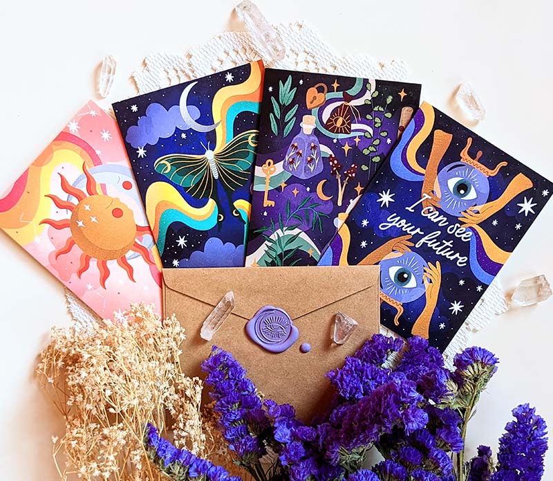 The 4 greeting cards fanned out so you could see each design. From left to right: Sun and Moon embraced, moth flying in the night sky, magical potions, and the "I can see your future" card that has crystal ball with eye.