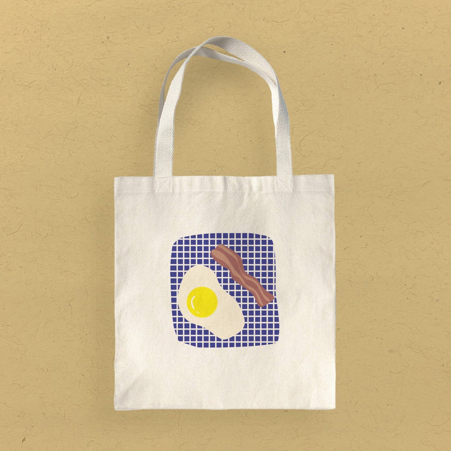 Canvas Tote bag featuring a blue and white grid background with a fried egg and one slice of bacon. Available on Kangyco.com.