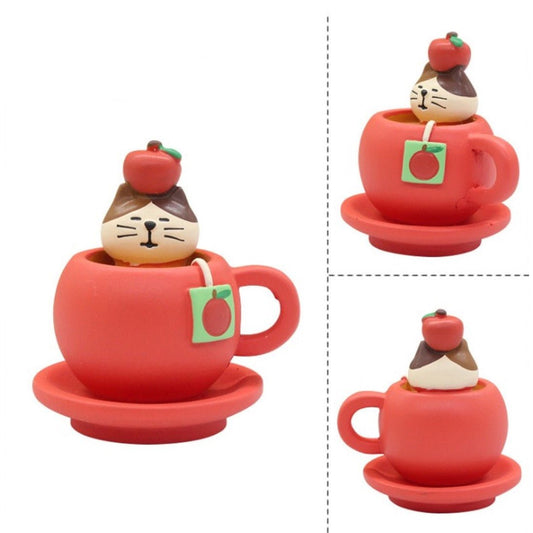 Pawsome cat figurine with an apple on the top of its head inside of a red mug and saucer with a tea bag of an apple.