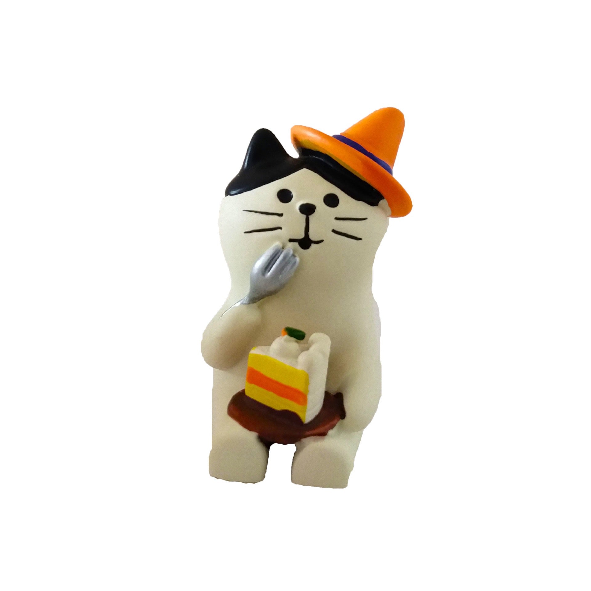 Adorable Pawsome figurine of a white cat with black ears sitting with an orange witch hat on one ear, a fork to its mouth, a slice of cake