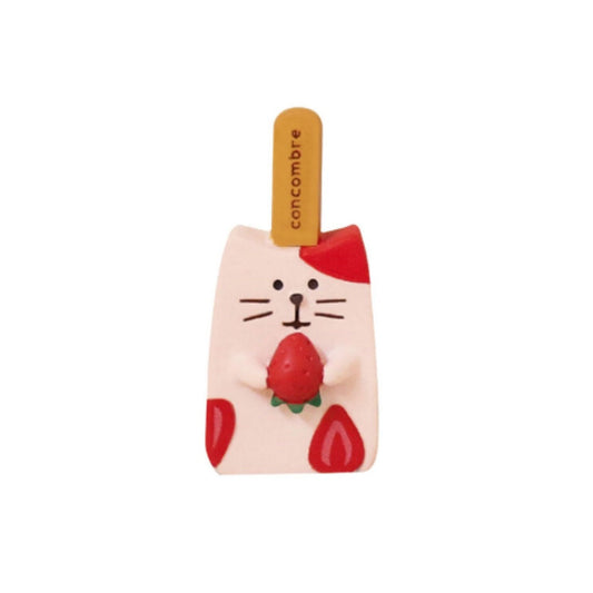 A strawberry popsicle Pawsome figurine holding a strawberry in its hands and the popsicle stick reads "concombre" made from polymer clay.