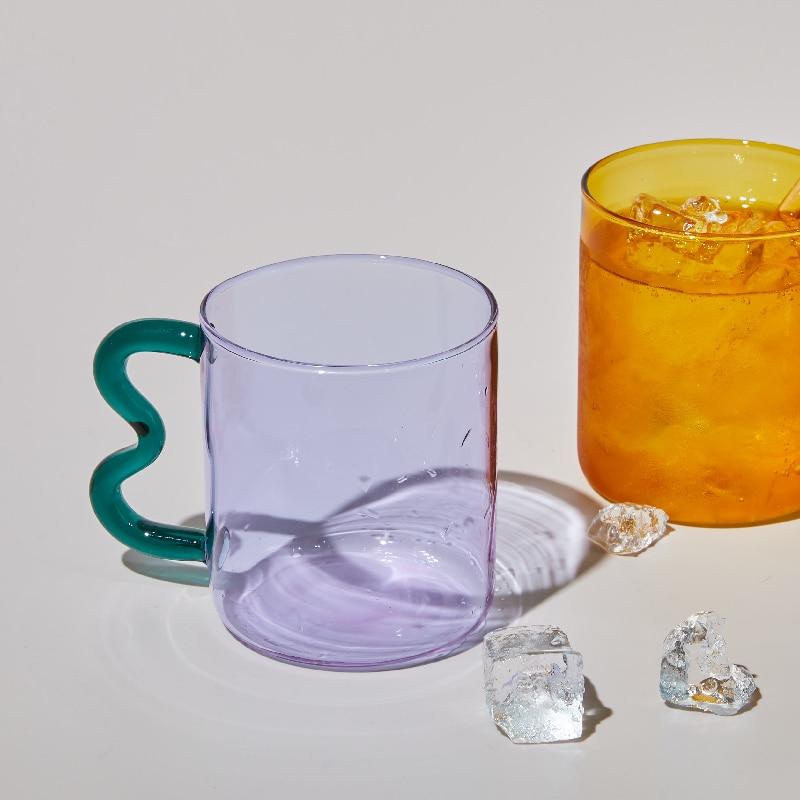 The style C of purple translucent glass mug with the wavy handle in green next to the yellow translucent glassware.